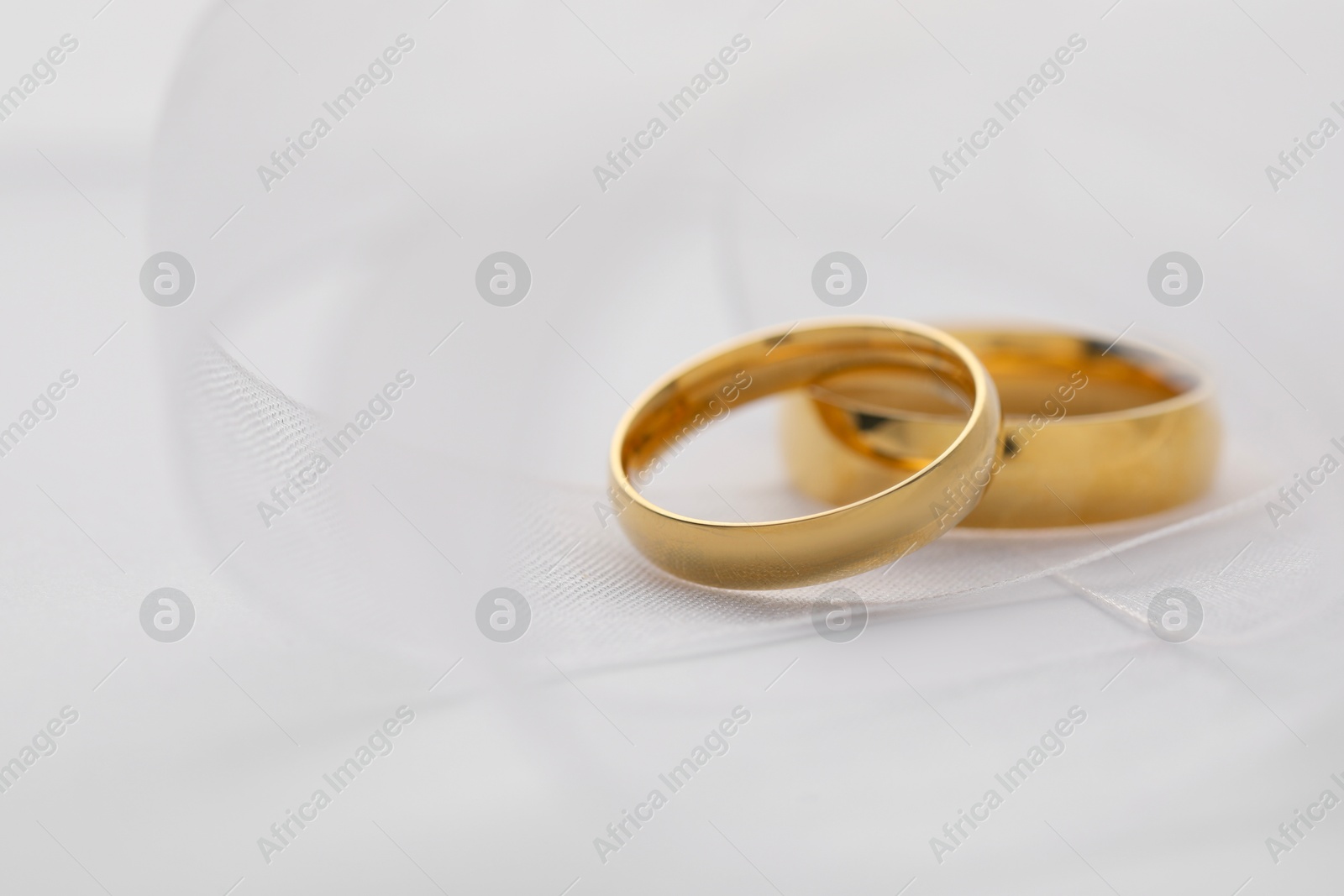 Photo of Beautiful golden wedding rings and ribbon on white background, closeup