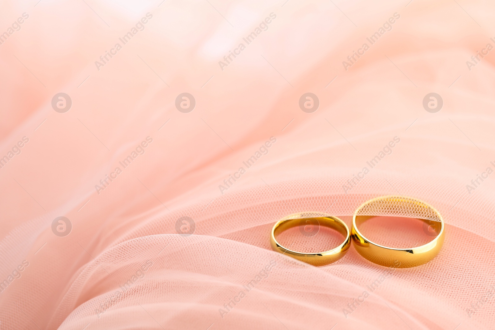 Photo of Beautiful golden wedding rings on pink fabric, space for text