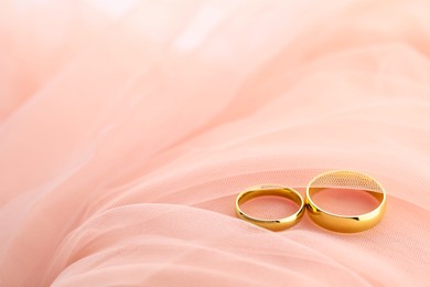 Beautiful golden wedding rings on pink fabric, space for text