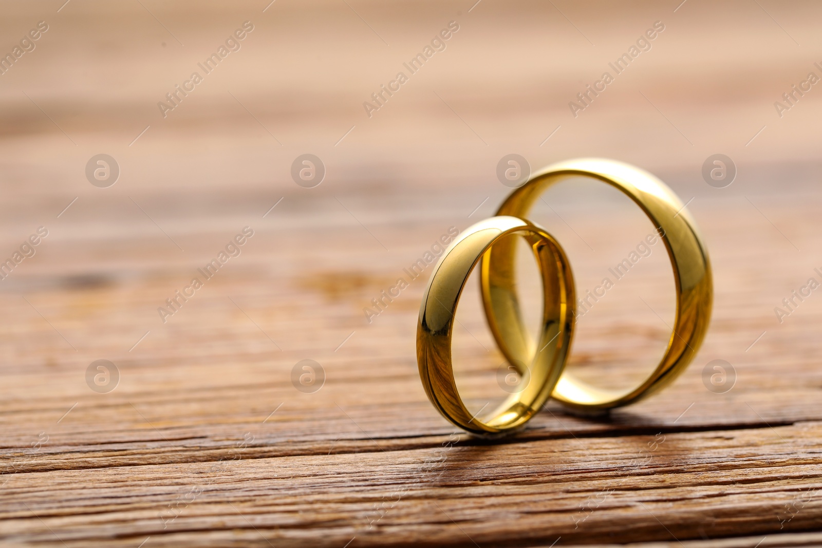 Photo of Beautiful golden wedding rings on wooden background, closeup. Space for text