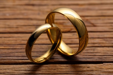 Photo of Beautiful golden wedding rings on wooden background, closeup