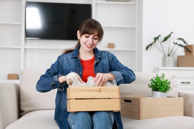 Photo of Happy woman holding wooden crate with stuff in new apartment. Housewarming party