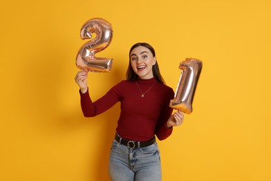 Photo of Coming of age party - 21st birthday. Happy young woman with number shaped balloons on yellow background