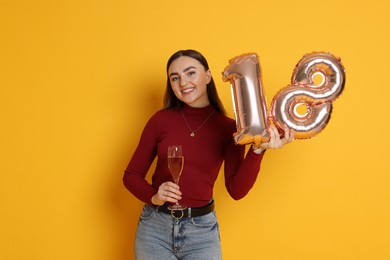 Photo of Coming of age party - 18th birthday. Happy young woman with number shaped balloons and glass of sparkling wine on yellow background