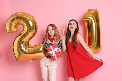 Photo of Coming of age party - 21st birthday. Young women celebrating with number shaped balloons on pink background