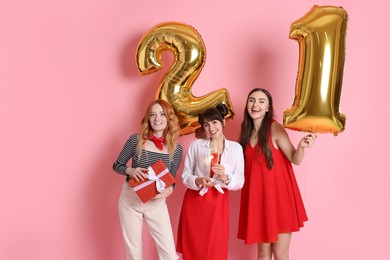 Coming of age party - 21st birthday. Group of young women celebrating with number shaped balloons on pink background