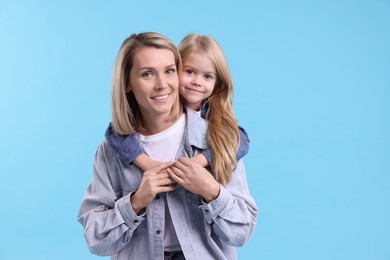 Photo of Cute little girl hugging her mom on light blue background. Happy Mother's Day