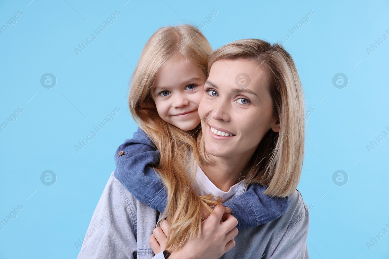 Photo of Cute little girl hugging her mom on light blue background. Happy Mother's Day