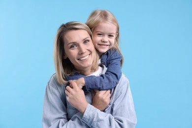 Photo of Cute little girl hugging her mom on light blue background. Happy Mother's Day