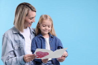 Photo of Little daughter congratulating her mom with greeting card on light blue background, space for text. Happy Mother's Day