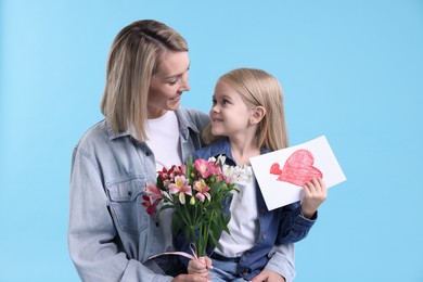 Photo of Little daughter congratulating her mom with bouquet of alstroemeria flowers and greeting card on light blue background. Happy Mother's Day