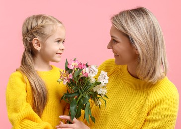 Photo of Little daughter congratulating her mom with bouquet of alstroemeria flowers on pink background. Happy Mother's Day