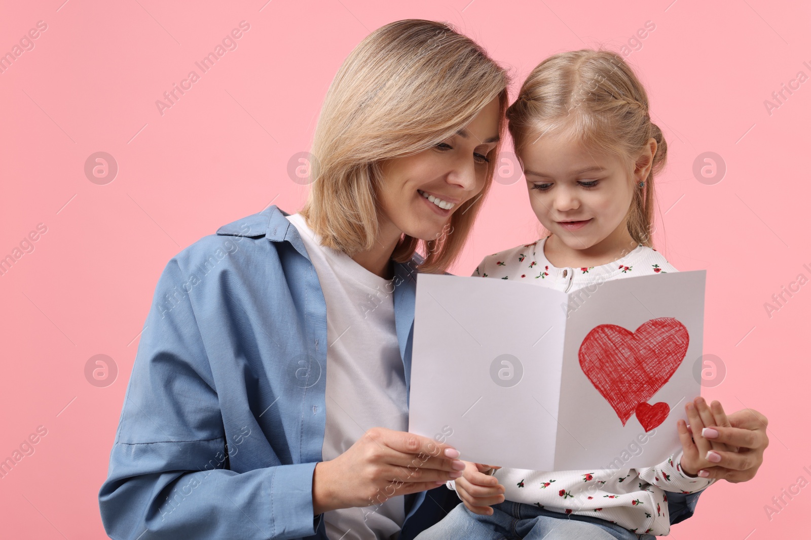 Photo of Happy woman with her daughter and greeting card on pink background. Mother's Day celebration