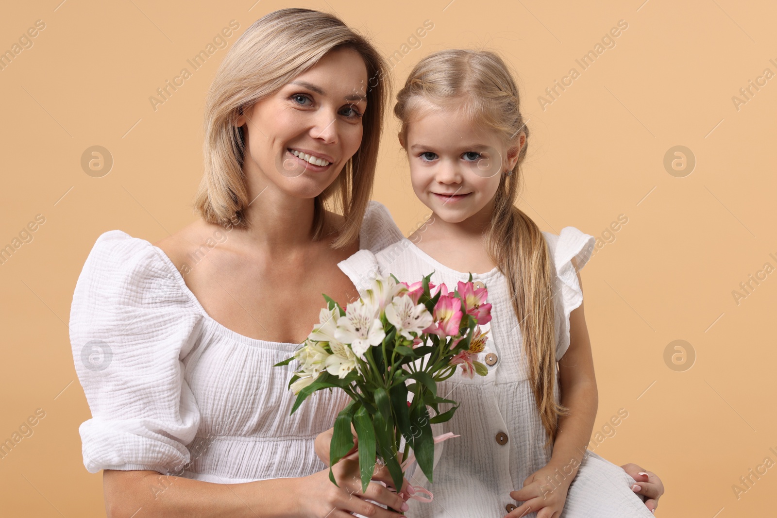 Photo of Happy woman with her daughter and bouquet of alstroemeria flowers on beige background. Mother's Day celebration