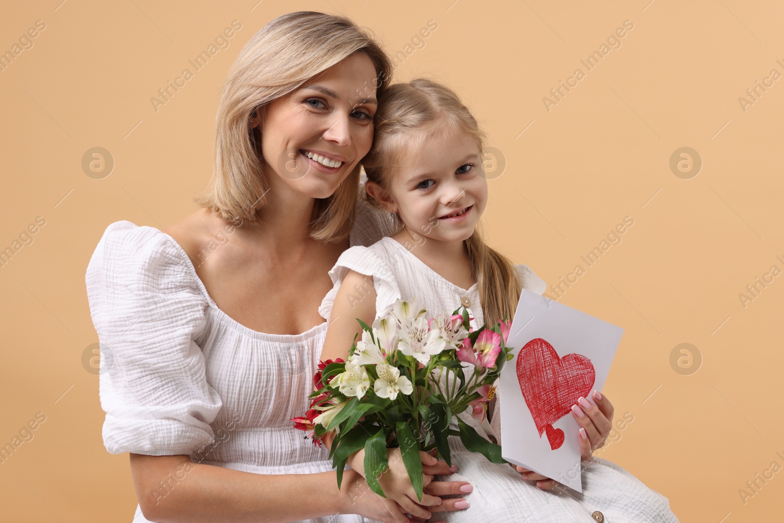 Photo of Happy woman with her daughter, bouquet of alstroemeria flowers and greeting card on beige background. Mother's Day celebration