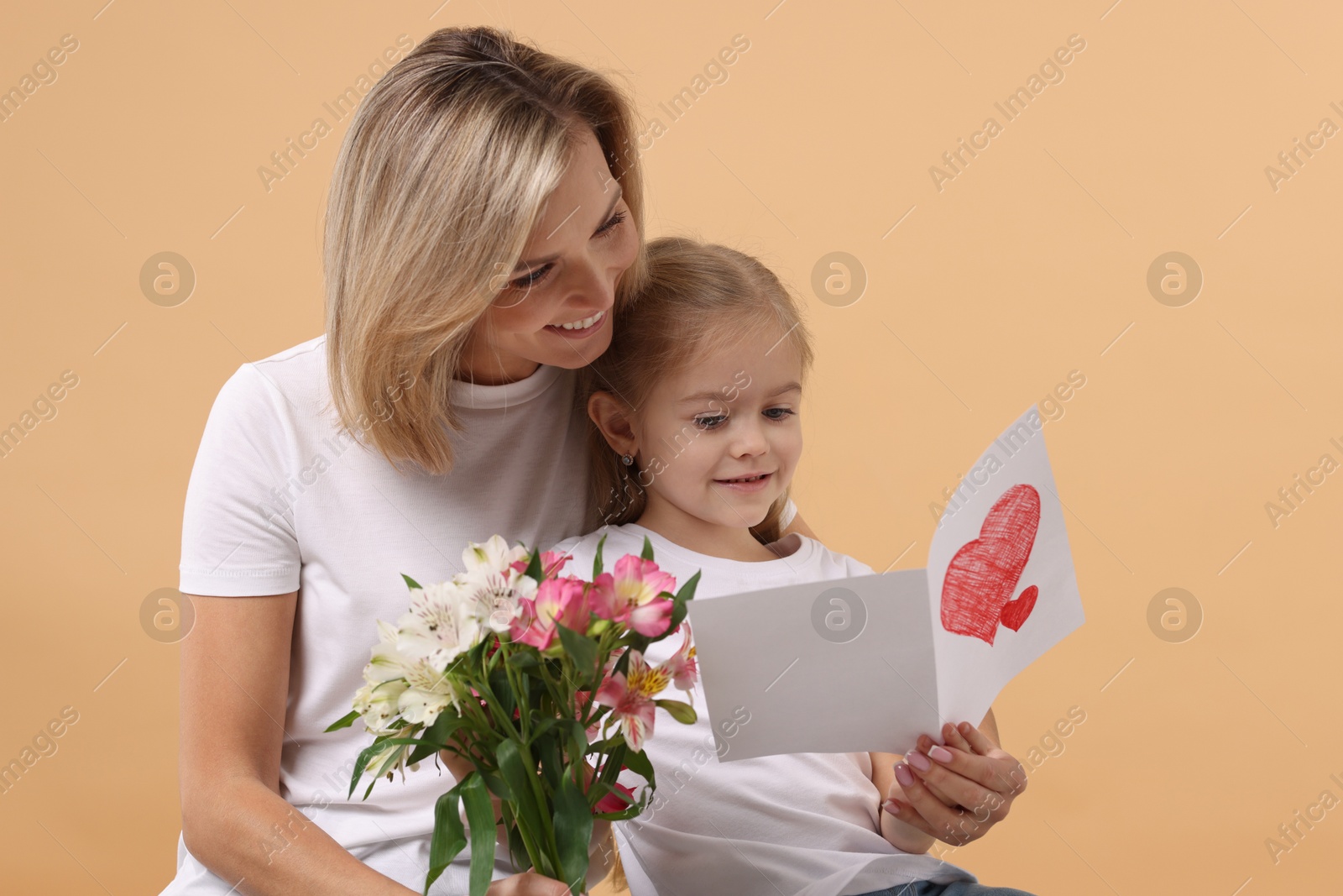 Photo of Happy woman with her daughter, bouquet of alstroemeria flowers and greeting card on beige background. Mother's Day celebration