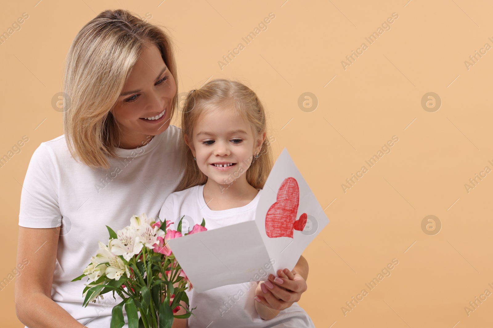 Photo of Happy woman with her daughter, bouquet of alstroemeria flowers and greeting card on beige background, space for text. Mother's Day celebration