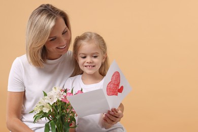 Photo of Happy woman with her daughter, bouquet of alstroemeria flowers and greeting card on beige background, space for text. Mother's Day celebration