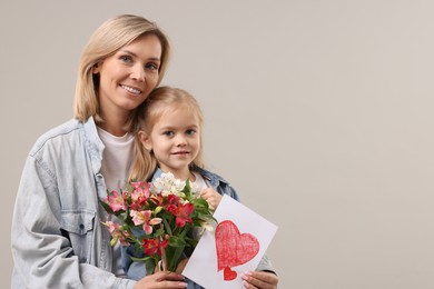 Photo of Happy woman with her daughter, bouquet of alstroemeria flowers and greeting card on gray background, space for text. Mother's Day celebration