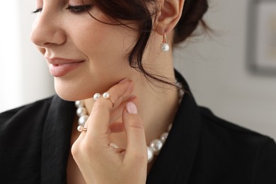 Beautiful young woman wearing elegant pearl jewelry indoors, closeup