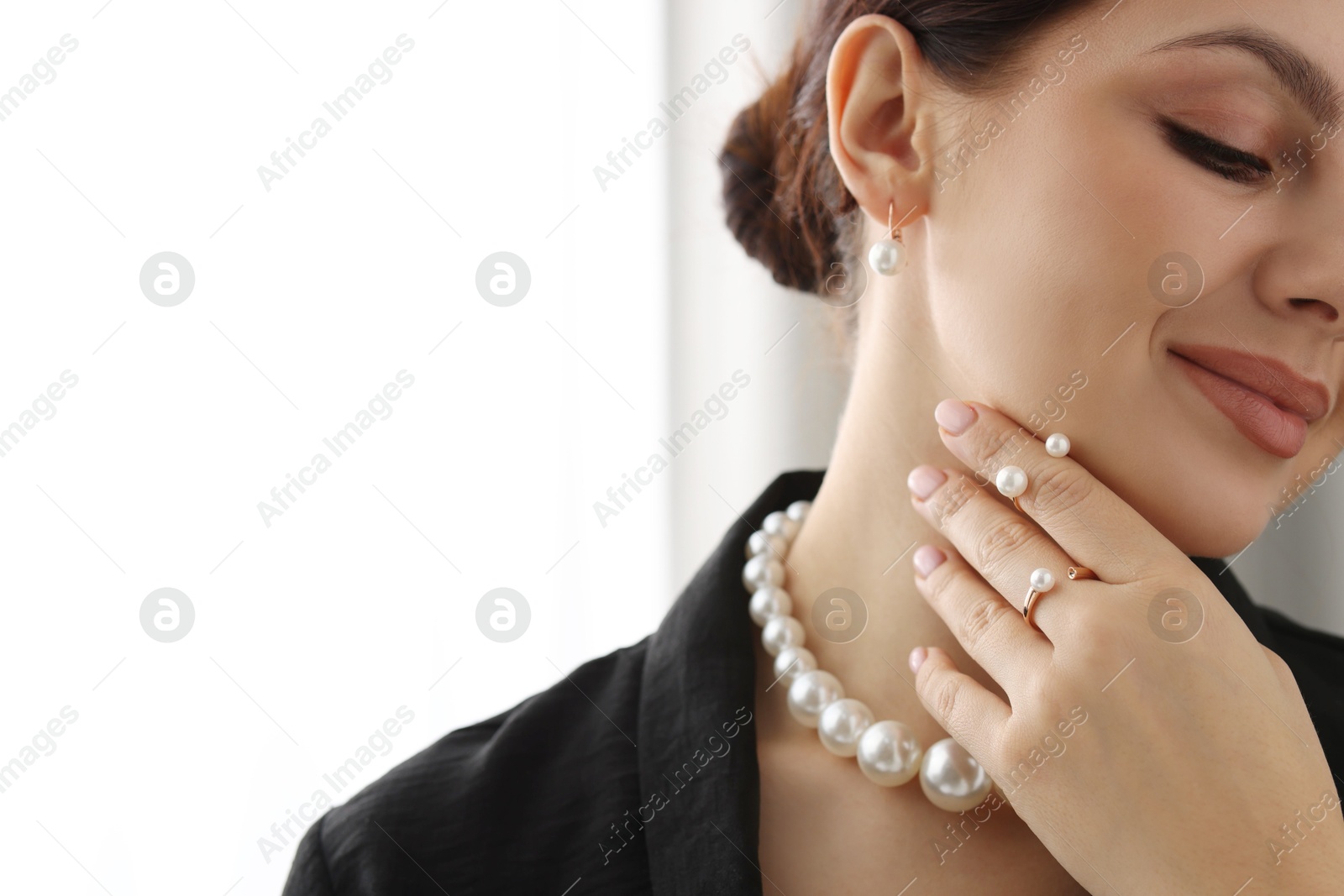 Photo of Young woman wearing elegant pearl jewelry indoors, closeup. Space for text