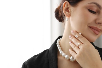 Photo of Young woman wearing elegant pearl jewelry indoors, closeup. Space for text