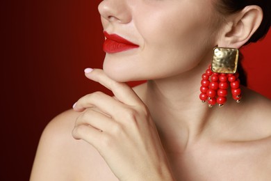 Beautiful young woman wearing elegant earrings on red background, closeup