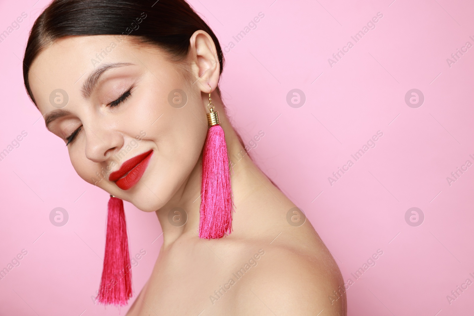 Photo of Beautiful young woman wearing stylish earrings on pink background. Space for text