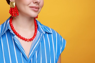 Photo of Young woman wearing stylish earrings and necklace on orange background, closeup. Space for text