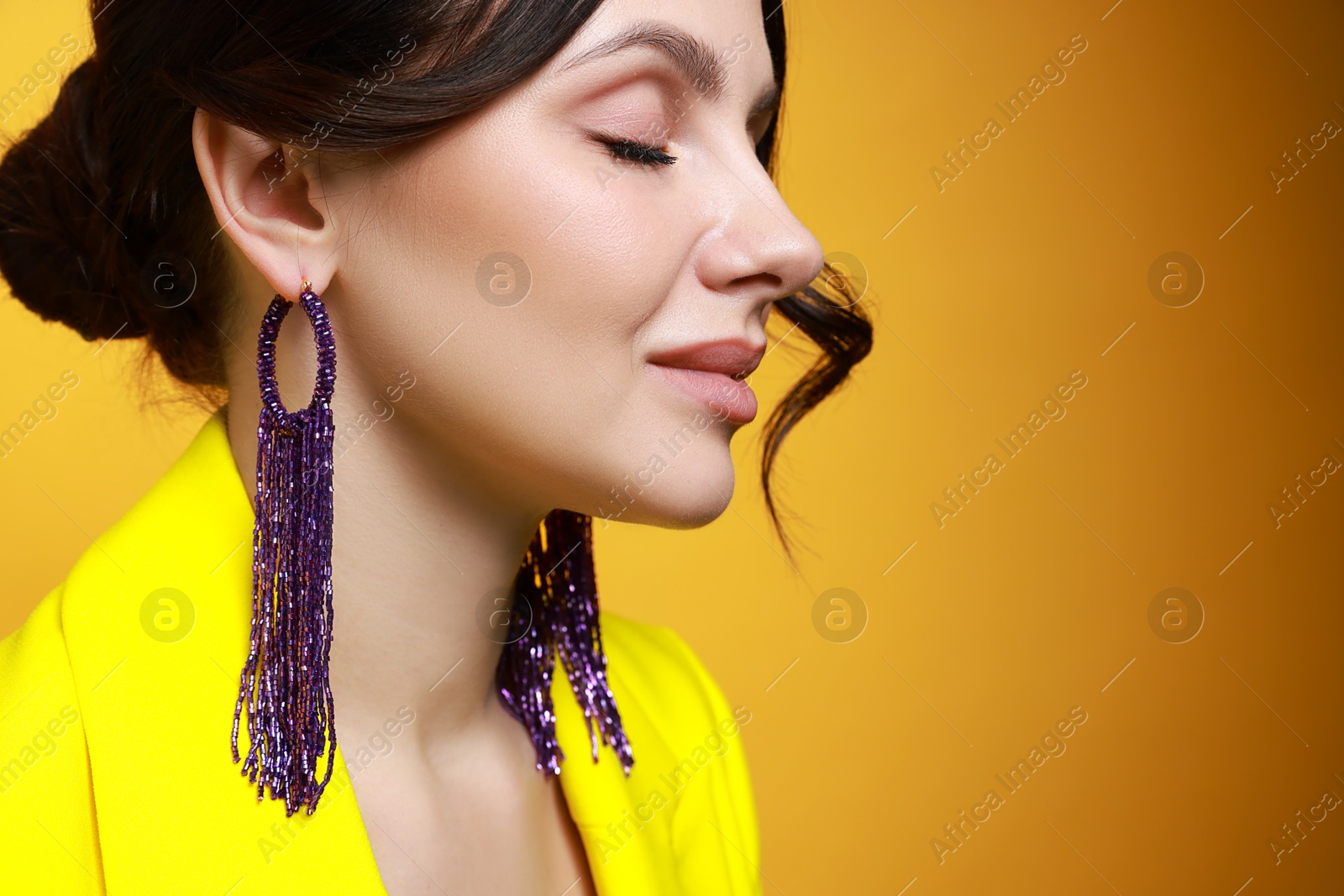 Photo of Beautiful young woman wearing stylish earrings on orange background, closeup. Space for text