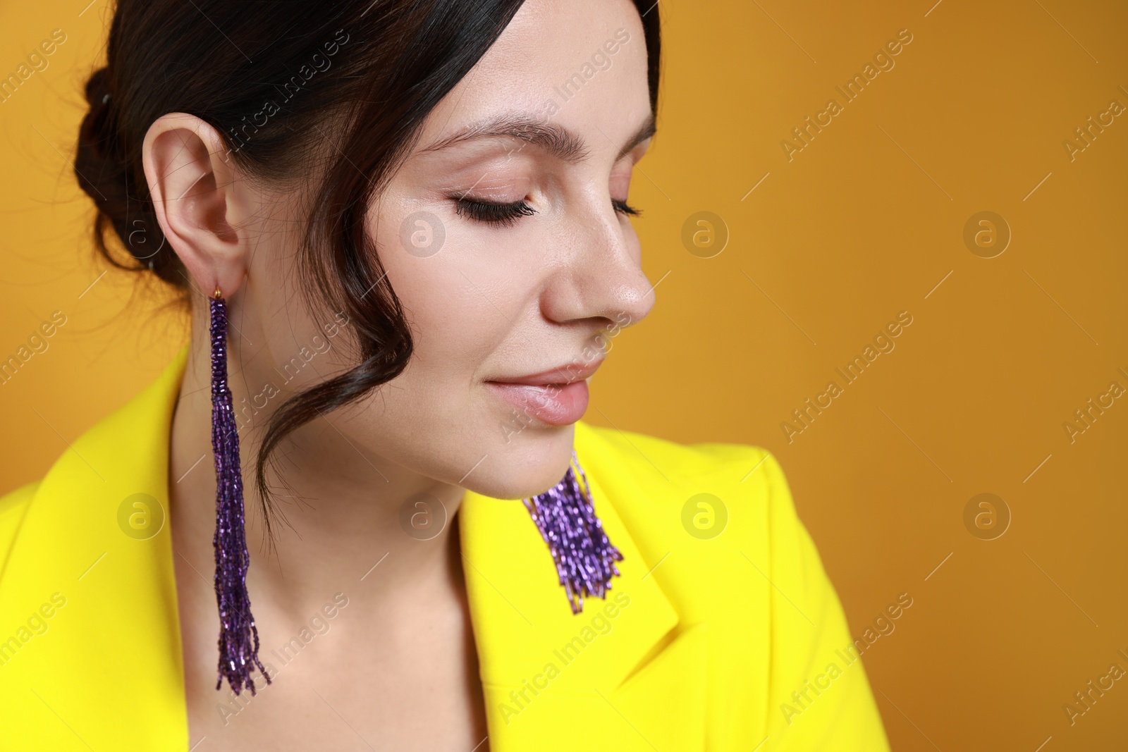 Photo of Beautiful young woman wearing stylish earrings on orange background, closeup. Space for text