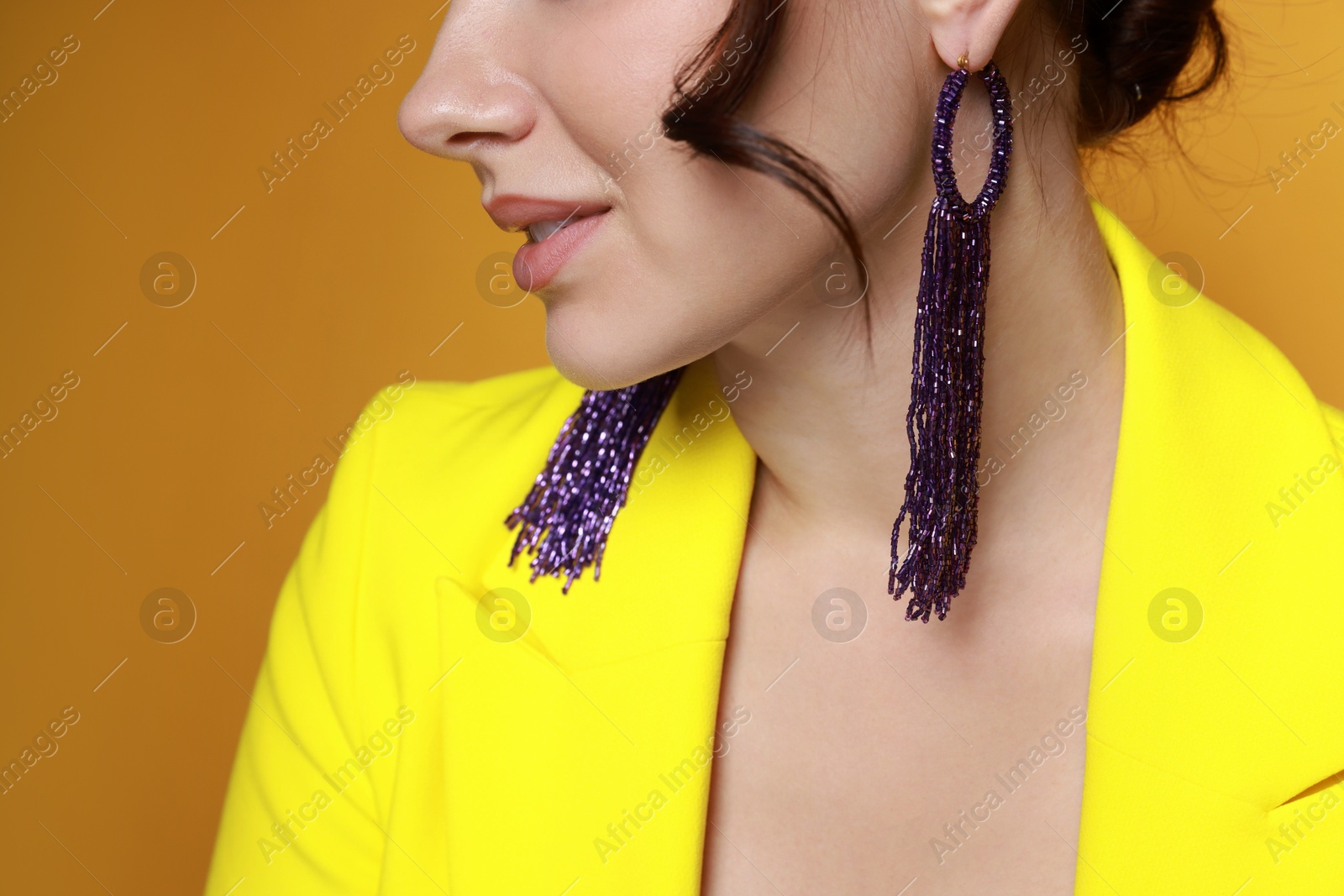 Photo of Woman wearing stylish earrings on orange background, closeup