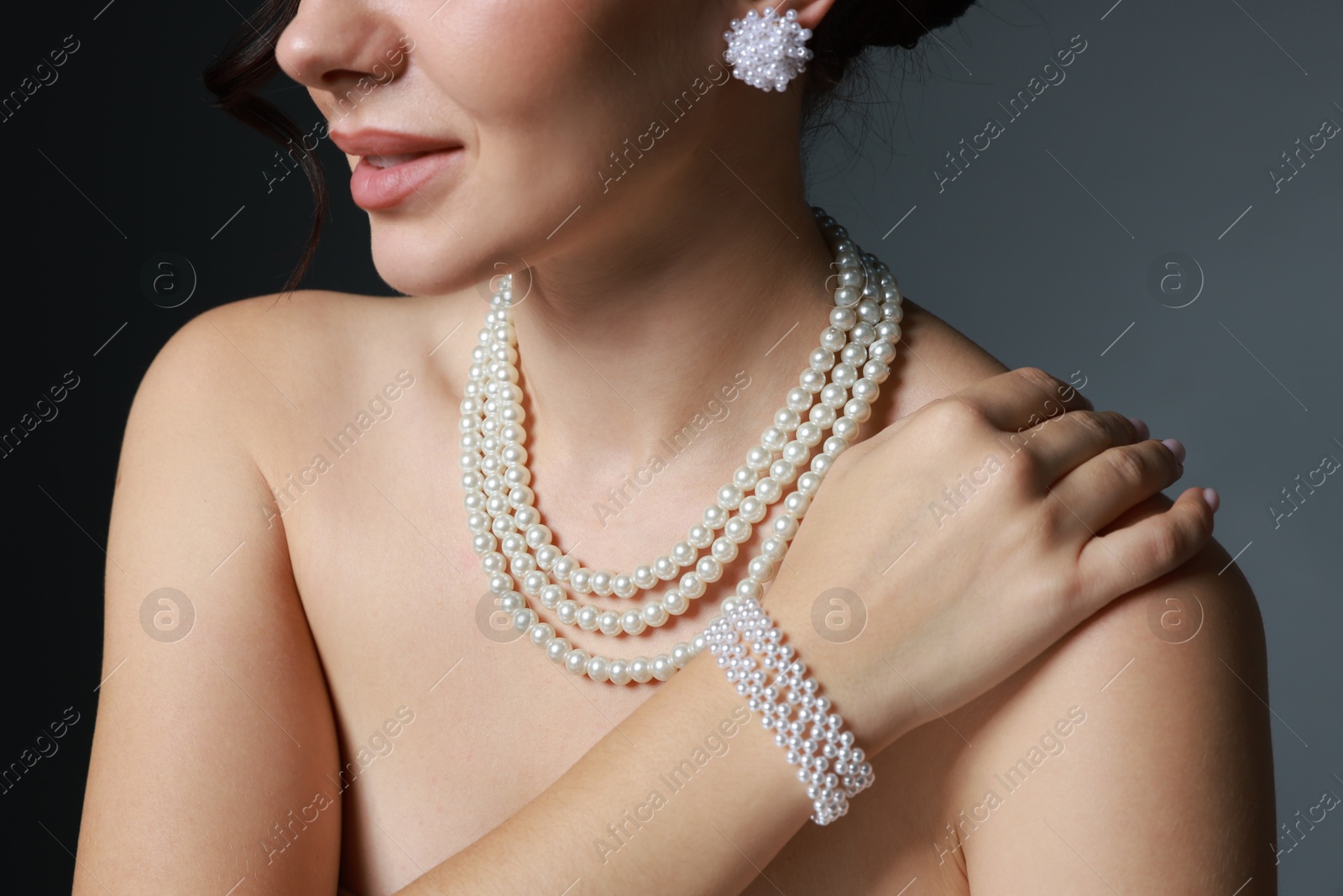 Photo of Woman wearing elegant pearl jewelry on dark grey background, closeup