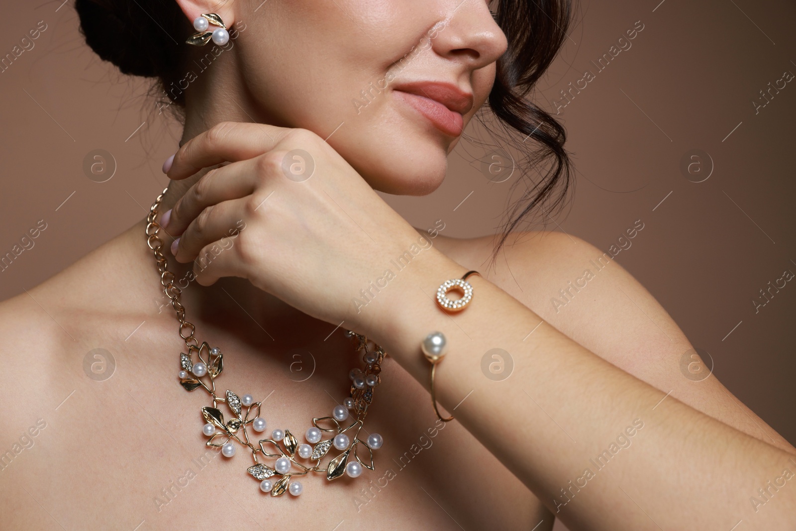 Photo of Young woman wearing elegant jewelry on brown background, closeup