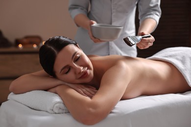 Photo of Chocolate body wrap. Spa worker applying mask onto woman's back in salon, closeup