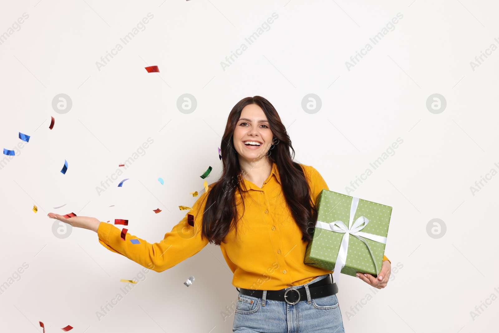 Photo of Happy woman with gift box and flying confetti on white background. Surprise party