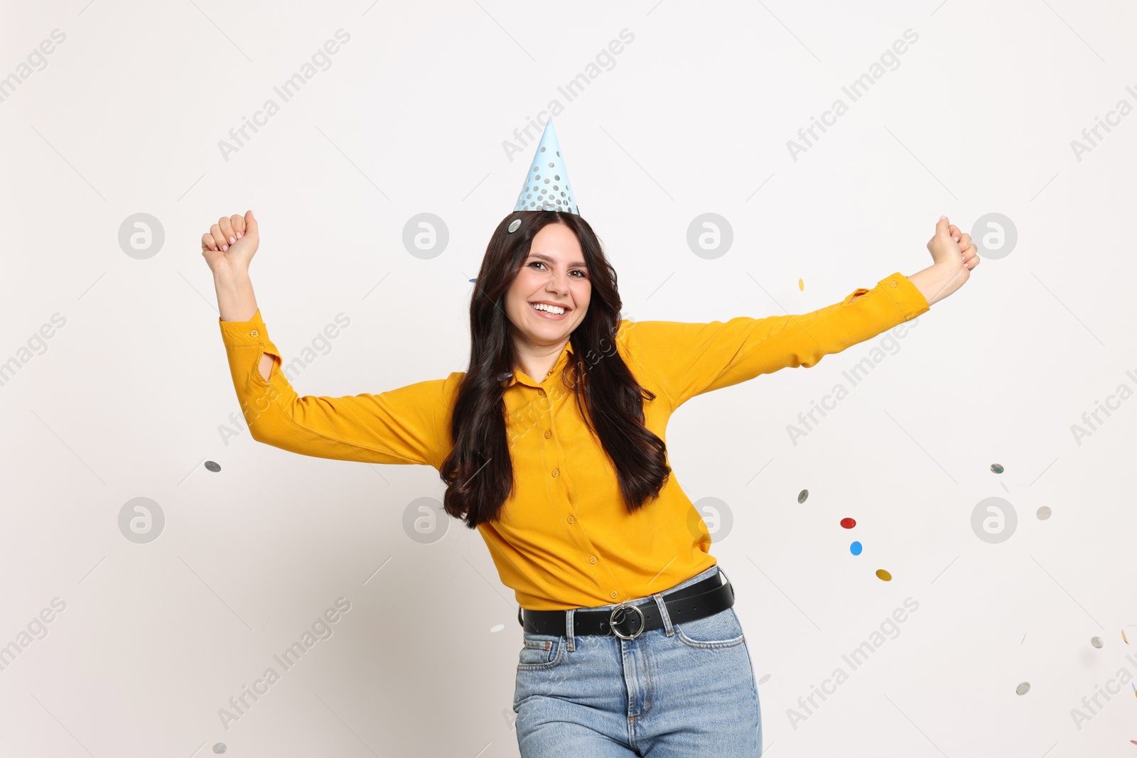 Photo of Happy woman in conical paper hat and flying confetti on white background. Surprise party