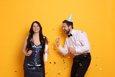 Photo of Happy friends having fun and flying confetti on orange background. Surprise party