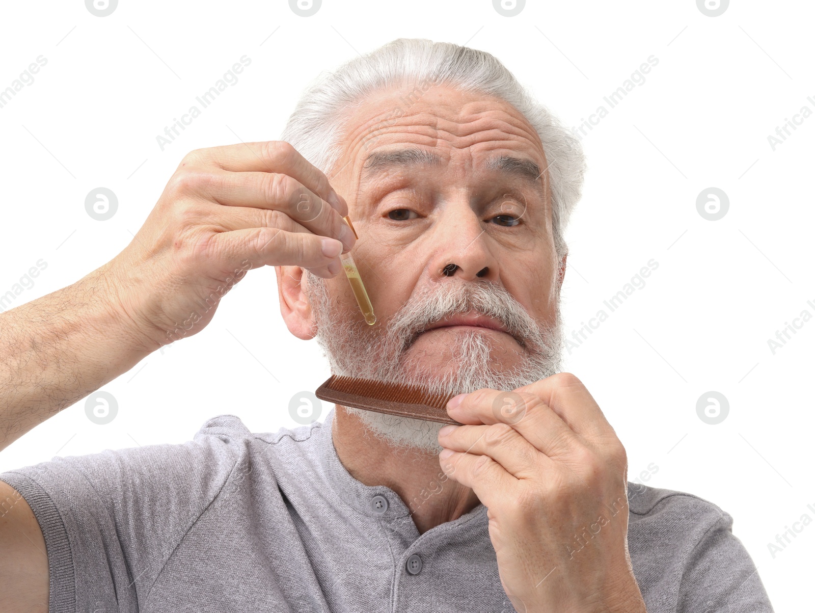 Photo of Senior man with comb applying oil onto his beard on white background