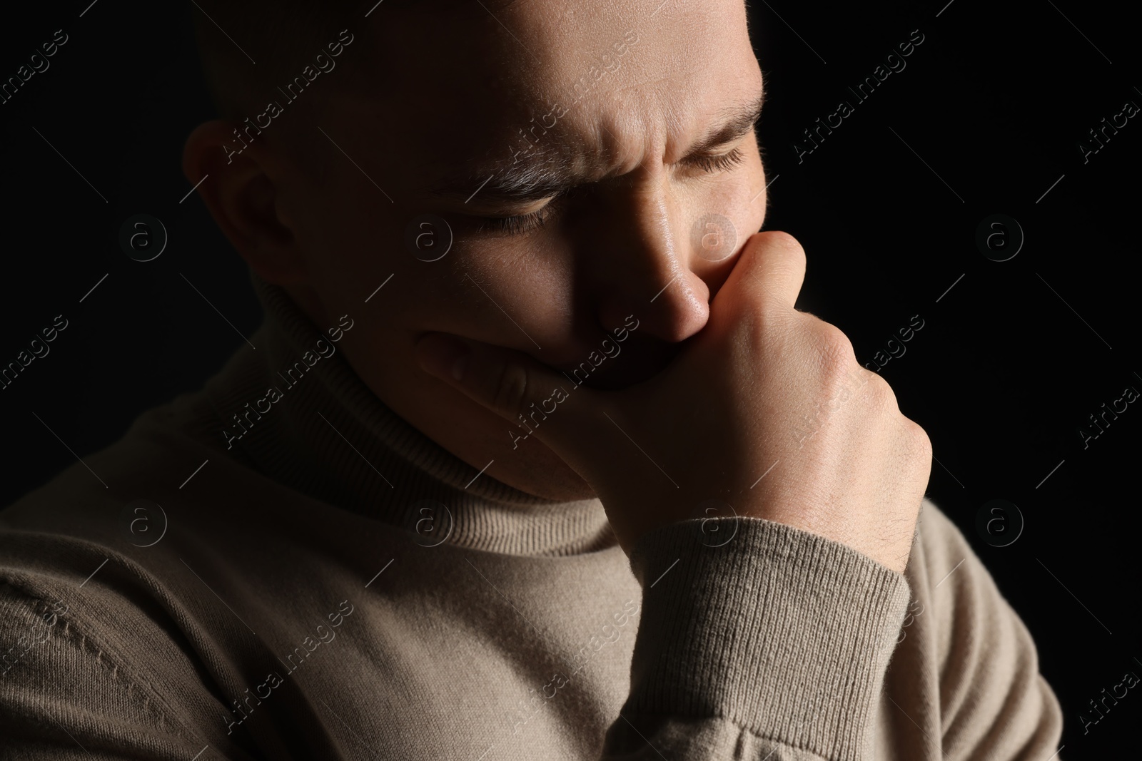 Photo of Distressed young man crying on black background, closeup