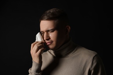 Photo of Crying man wiping tears with tissue on black background