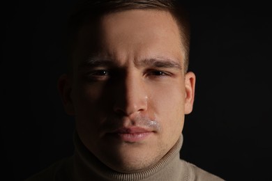 Distressed young man crying on black background, closeup