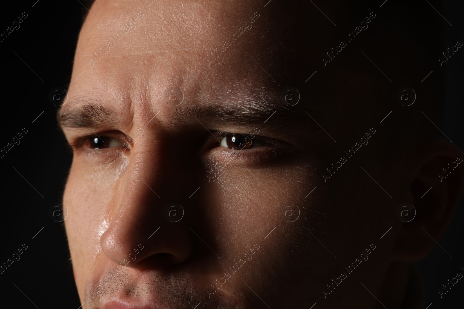 Photo of Distressed young man crying on black background, closeup