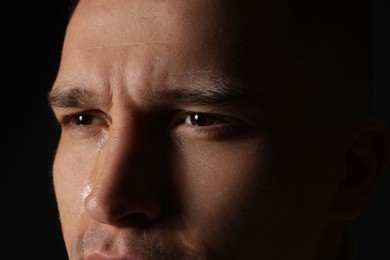 Distressed young man crying on black background, closeup