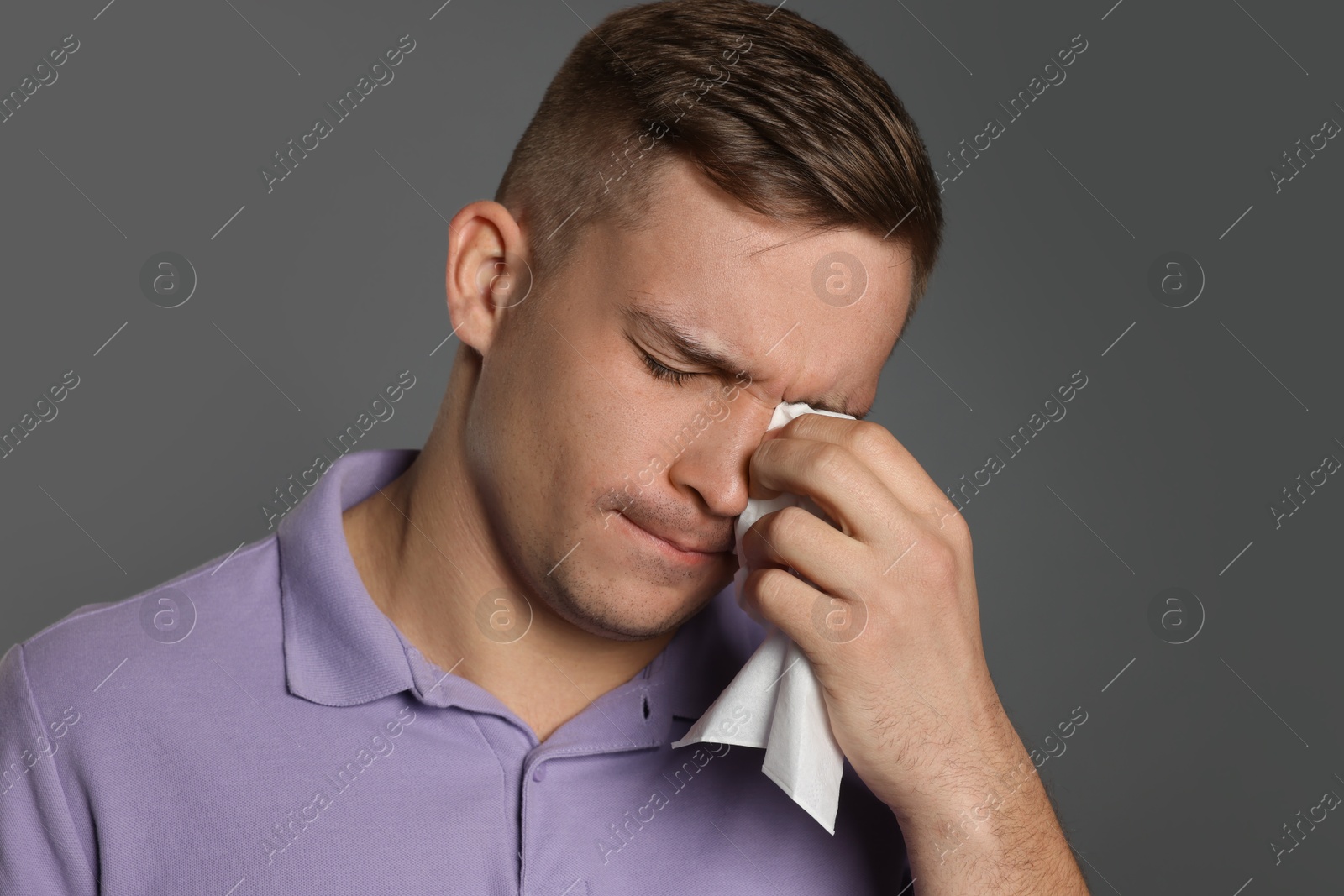 Photo of Crying man wiping tears with tissue on grey background