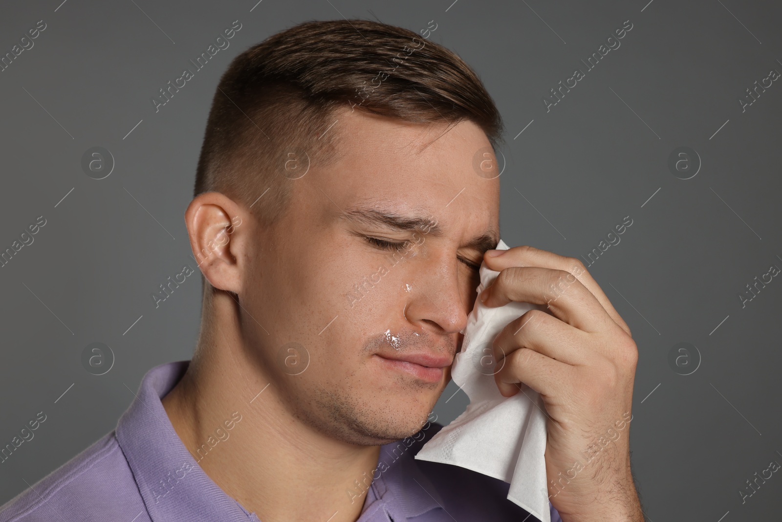 Photo of Crying man wiping tears with tissue on grey background