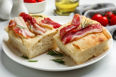 Photo of Pieces of delicious focaccia bread with bacon served on white table, closeup