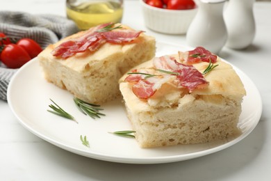 Photo of Pieces of delicious focaccia bread with bacon served on white table, closeup