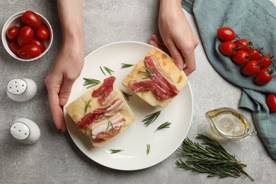 Photo of Woman serving delicious focaccia bread at grey table, top view