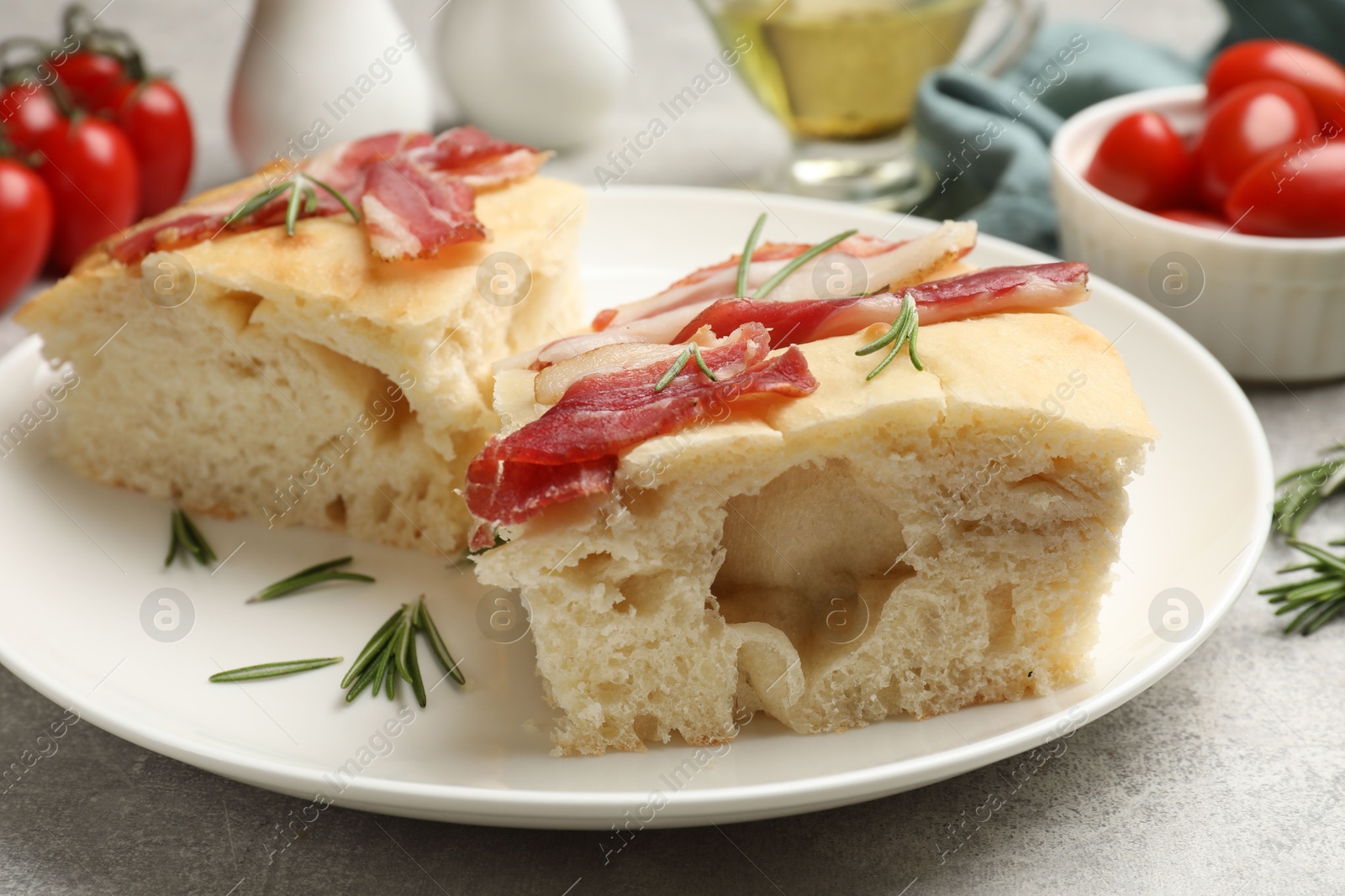 Photo of Pieces of delicious focaccia bread with bacon served on grey table, closeup